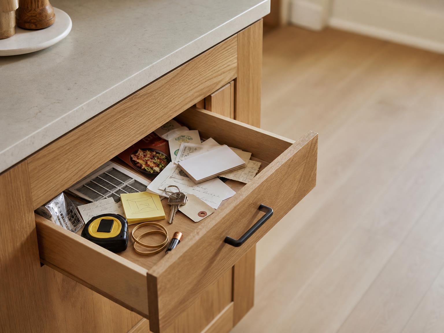 An open kitchen junk drawer holding a business card, a folded receipt, a spare key with a tag, handwritten notes and a sticky note with a measurement on it